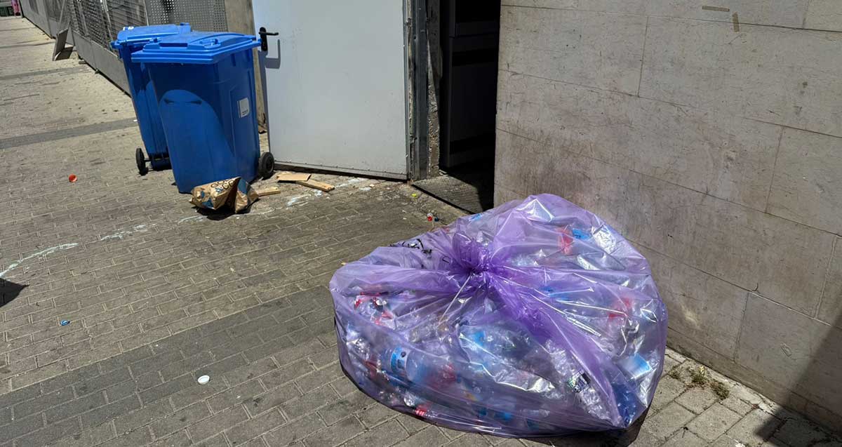 זבל זרוק במרכז הרצליה. שקית פלסטיק גדולה בצבע סגול על המדרכה ליד פתח של חדר אשפה. שני פחים כחולים ואשפה לידם ניצבים ליד חדר האשפה.