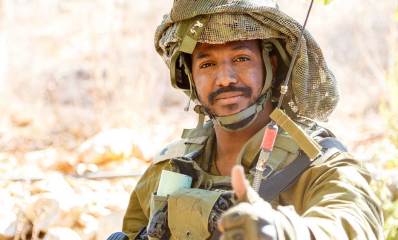 משה וורקו במדי צה"ל ודרגות רס"ן. עם קסדה ועליה רשת הסוואה, ואנטנה של מכשיר קשר בחזית.