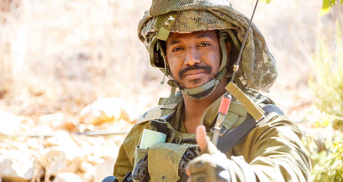 משה וורקו במדי צה"ל ודרגות רס"ן. עם קסדה ועליה רשת הסוואה, ואנטנה של מכשיר קשר בחזית.