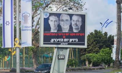 שילוט חוצות על שטח הפרדה בין נתיבים ברעננה. לצידו דגל ישראל ודגל עיריית רעננה. בשלט כתוב: הקרנת טקס יום הזיכרון הפסלטיני = ביזיום יום הזיכרון. לטפולכם. בשלט תמונת ראש העיר וסגניו