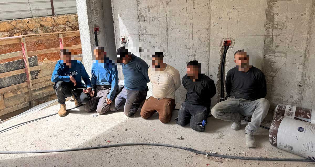 שישה שב"חים באתר בנייה בהרצליה, על הברכיים ואזוקים בידיים מאחורי הגב. הפנים מטושטשות.