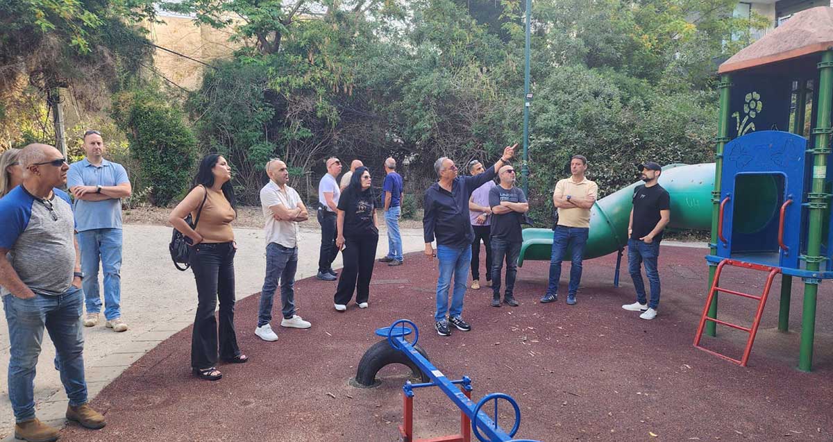 סיור של עובדי אגף התפעול בעיריית רמת השרון. הם עומדים בגן שעשועים, סביב רוכברגר המצביע כלפי מעלה.