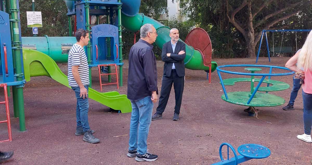 רוכברגר וקורצקי לא משחקים. שניהם ועוד עובד עומדים במרכז גן משחקים.