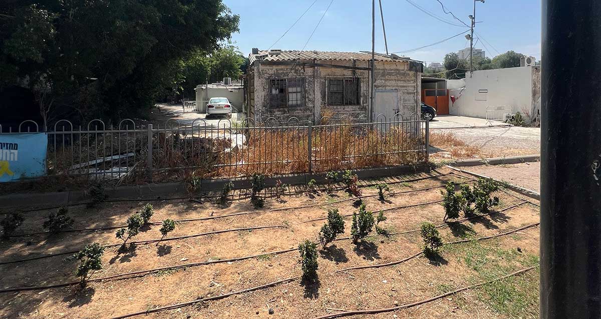 צריף האסבסט ברחוב דוד אלקלעי בשכונת נווה ישראל. דלת ושני חלונות מסורגים בחזית. גג אסבסט משופע.