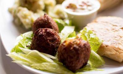 פלאפל בצלחת. שלושה כדורי פלאפל מונחים על עלי חסה בצלחת גדולה. ליד הפלאפל פיתה עם ממרח. על הצלחת קופסת פלסטיק עגולה עם מאכל בתוכה.