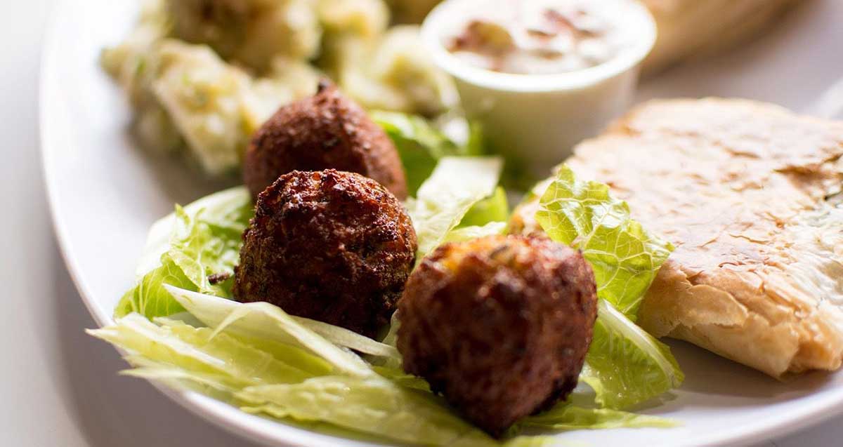 פלאפל בצלחת. שלושה כדורי פלאפל מונחים על עלי חסה בצלחת גדולה. ליד הפלאפל פיתה עם ממרח. על הצלחת קופסת פלסטיק עגולה עם מאכל בתוכה.