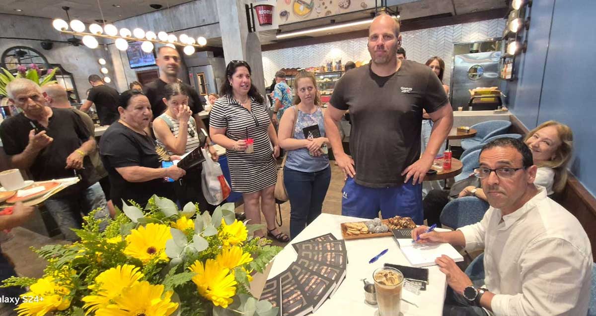 עשרות ממתינים בתור להקדשה של אלי שרעבי אשר יושב ליד שולחן וחותם.
