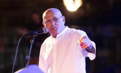 ממה שיינפיין חבר מועצת עיריית כפר סבא, ממושקף ובחולצה לבנה, עומד ליד מיקרופון ויד שמאל מצביעה קדימה.