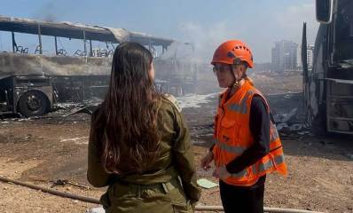 זירת נפילת הטיל האיראני בהרצליה בבוקר 17 ביוני 2025. כבאית וקצינת צה"ל ליד אוטובוס שרוף.