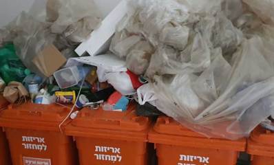 פחים כתומים בשכונת גליל ים מלאים ועליהם ערמות של אריזות עם פסולת למיחזור.