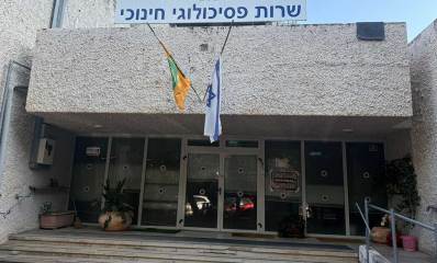 השירות הפסיכולוגי החינוכי של עיריית כפר סבא ברחוב נחשון 16. הכניסה לבניין רחבה עם דלתות ולוחות של זכוכית. מעל הכניסה שלט בכיתוב: שרות פסיכולוגי חינוכי, ומתחתיו דגל המדינה ודגל העיר.