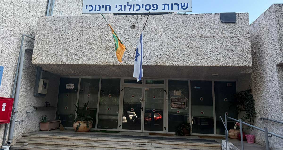 השירות הפסיכולוגי החינוכי של עיריית כפר סבא ברחוב נחשון 16. הכניסה לבניין רחבה עם דלתות ולוחות של זכוכית. מעל הכניסה שלט בכיתוב: שרות פסיכולוגי חינוכי, ומתחתיו דגל המדינה ודגל העיר.