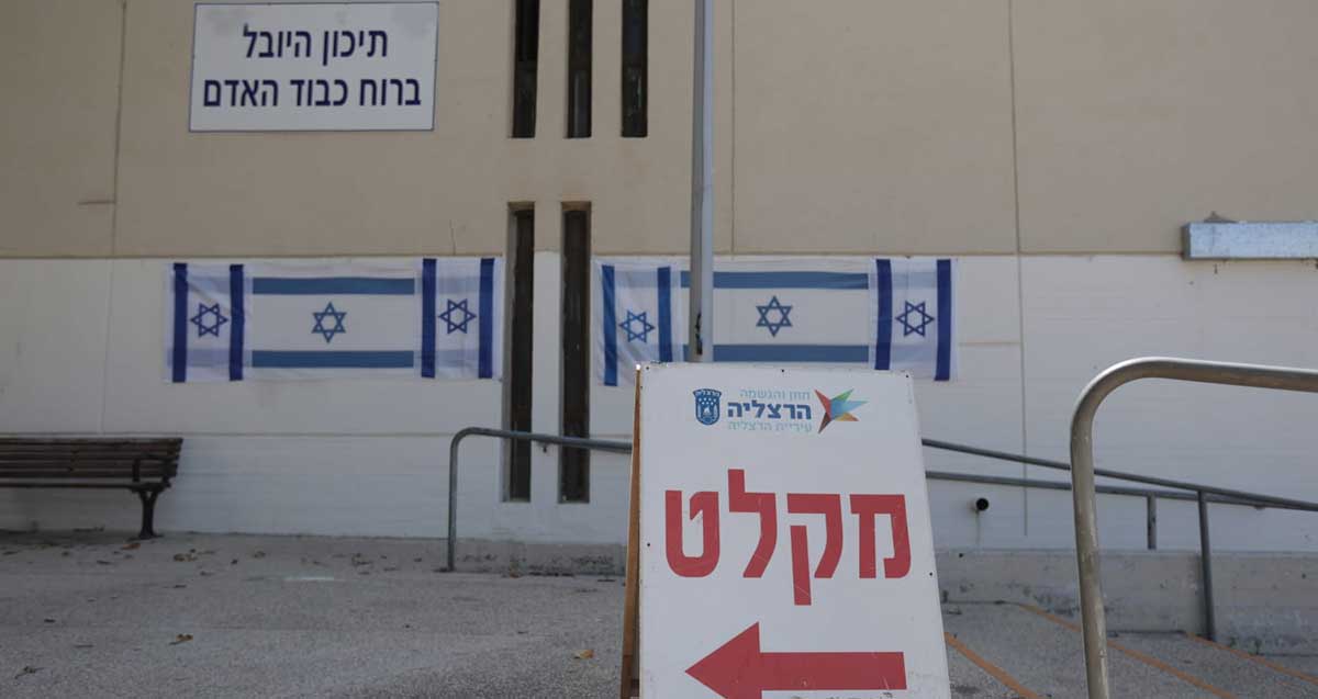 מקלט ציבורי בבית ספר. שלט בחוץ עם חץ שמאלה וכיתוב: מקלט. על קיר הבניין הכיתוב: תיכון היובל ברוח כבוד האדם.