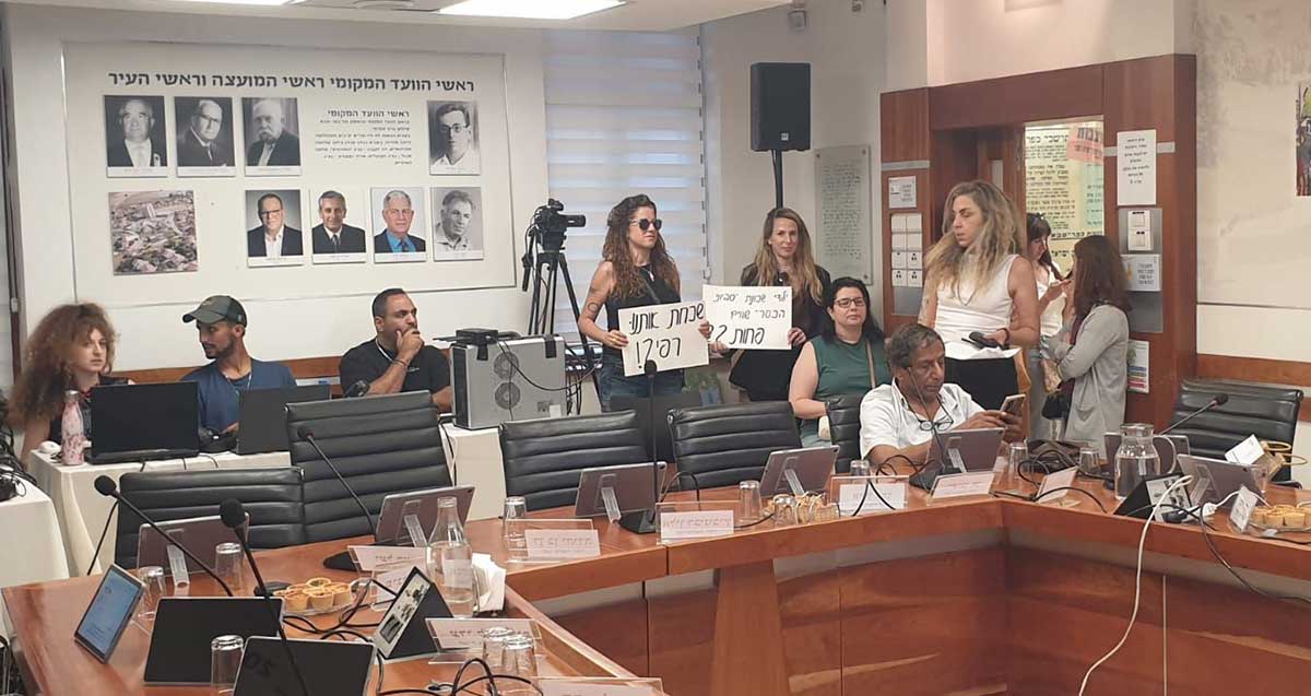 מחאת תושבי שכונת סביוני הכפר בישיבת מועצת עיריית כפר סבא. שתי תושבות עומדות עם שלטים מאחורי שולחן הישיבה. שלט אחד עם כיתוב: שכחת אותנו רפי?! שלט שני: ילדי שכונת 'סביוני הכפר' שווים פחות ??!