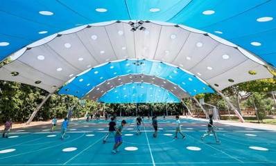 הצללה בבית הספר לפיד בהוד השרון, מעל מגרש ספורט גדול, סככות בצורת קשת. ילדים משחקים במגרש.