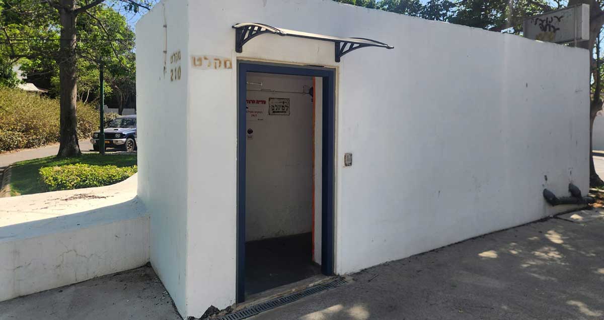 מקלט ציבורי על פני הקרקע. ליד הכניסה כיתוב: מקלט. מעבר לדלת יש שילוט ימינה למקלט, ושלט של עיריית הרצליה.