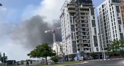 נפילת טיל בהרצליה. עשן עולה מאחורי מנוף של בניין בבניה ובניינים וכיכר בחזית