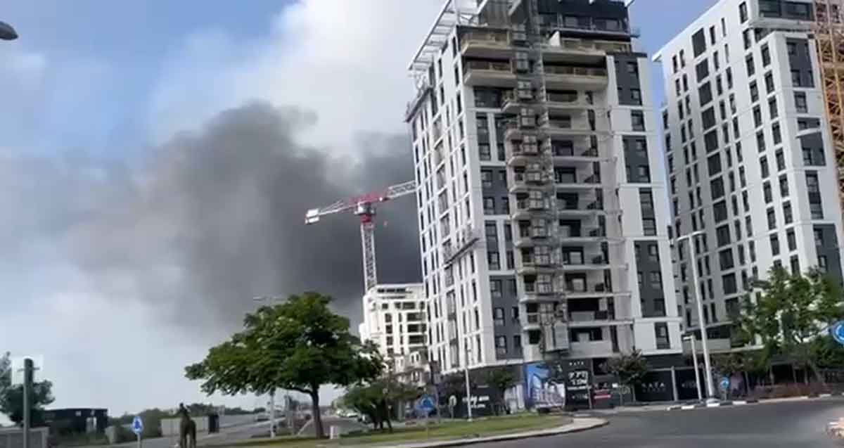 נפילת טיל בהרצליה. עשן עולה מאחורי מנוף של בניין בבניה ובניינים וכיכר בחזית