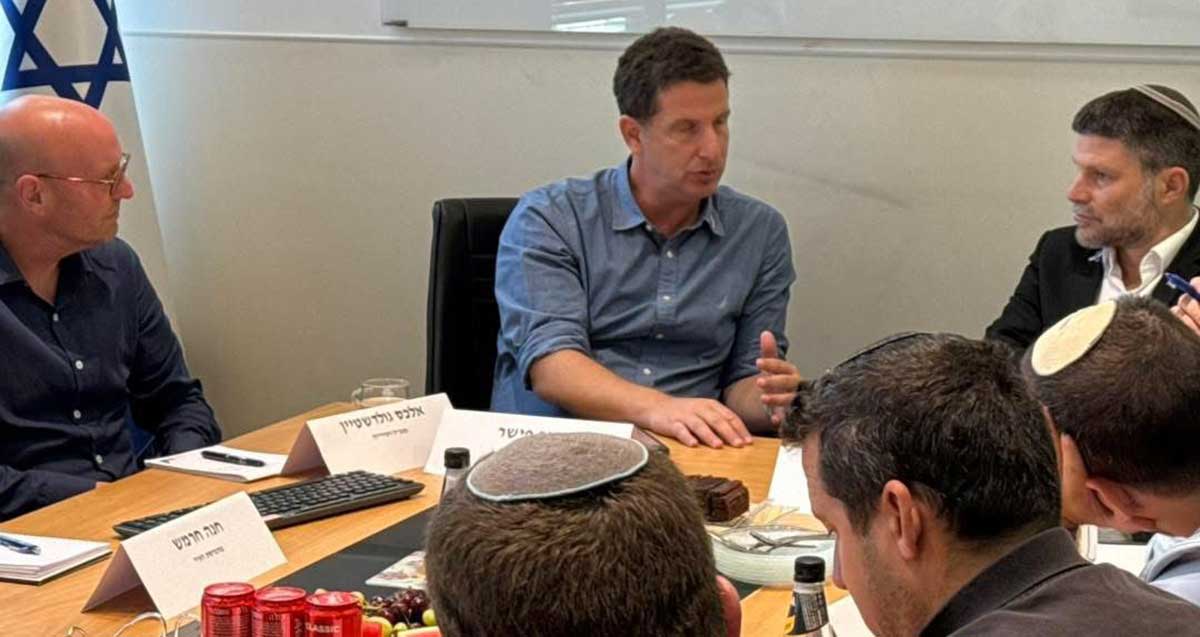 בצלאל סמוטריץ ויריב פישר יושבים בראש השולחן ואנשים נוספים בשני צידי השולחן. על השולחן פחיות קולה ופירות.