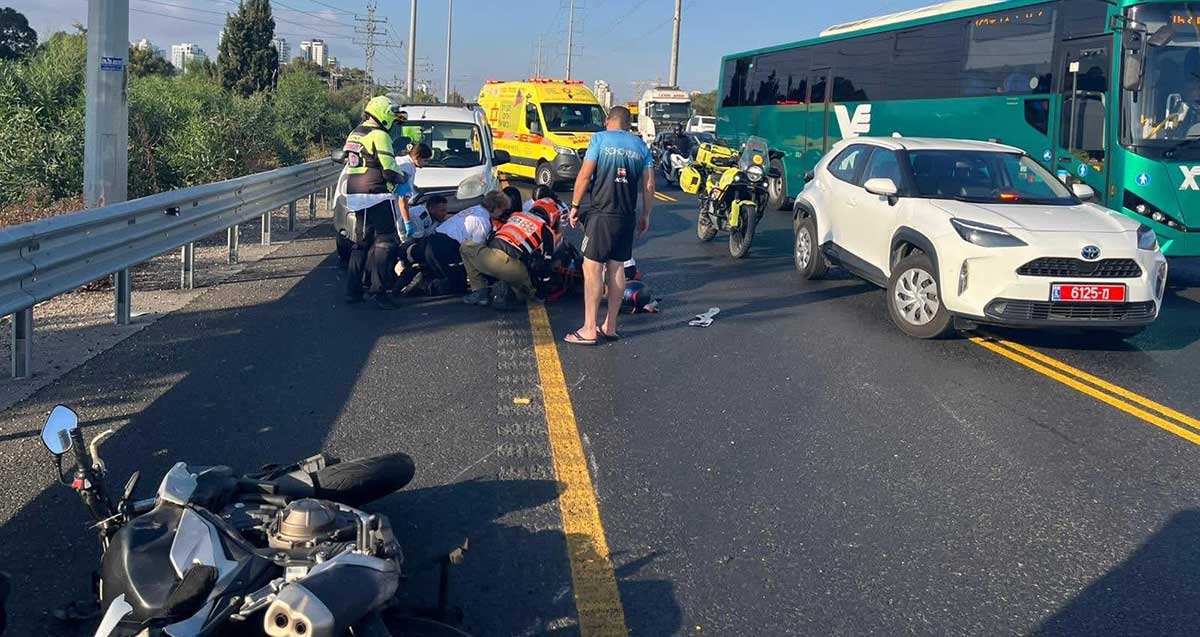 זירת התאונה בכביש 4. חובשים מטפלים בנפגע. מימין רכב משטרה. ברקע אמבולנס ואופנוע של מד"א, ובחזית אופנוע הפוך בשול הדרך.