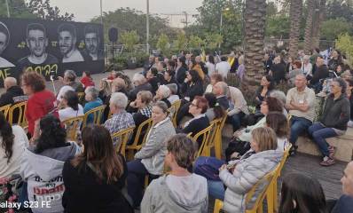 פעילות למען החטופים בכפר סבא. קהל רב יושב בגינה ציבורית מול מסך עליו מוקרנים תמונות ושמות של חטופים.