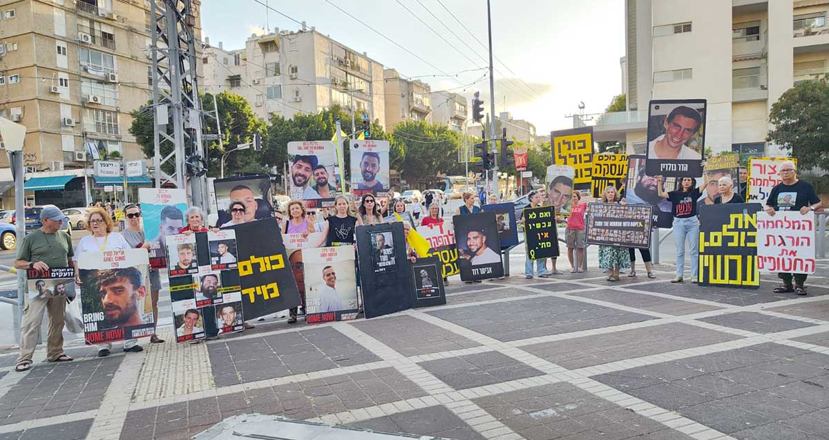 פעילות למען החטופים בכפר סבא. עשרות מפגינים עם שלטים ותמונות עומדים ברחבה. כיתוב בשלטים: כולם מיד, ואם לא עכשיו אין מתי, המלחמה הורגת את החטופים.