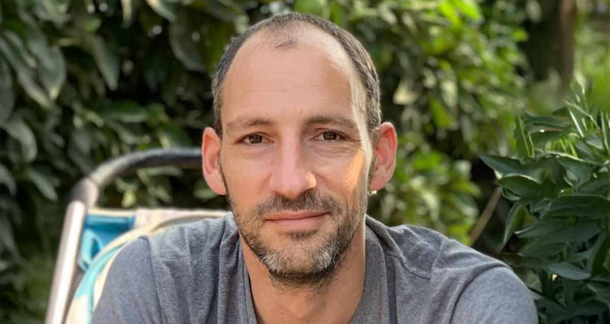 תמונת פנים של ארי נירון, מנהל בית הספר הדמוקרטי ע"ש יאנוש קורצ'אק. מאחוריו צמחייה