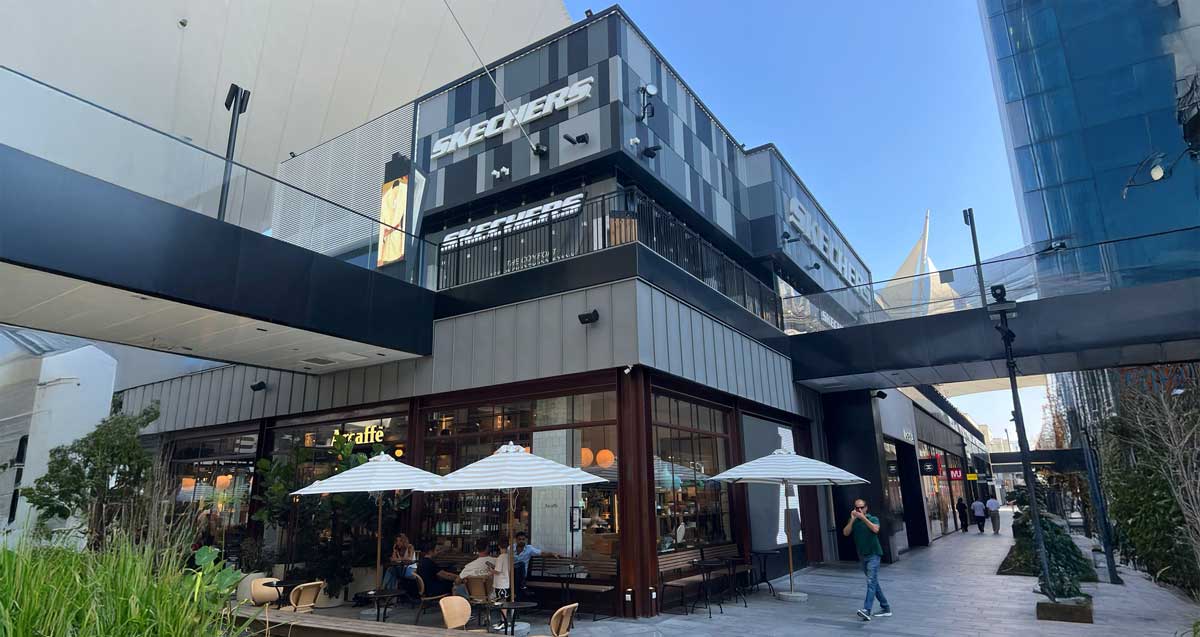 ביג פאשן גלילות. שתי שורות של חנויות בשתי קומות וביניהן רחבה לא מקורה עם גינות, שולחנות, כיסאות וספסלים.