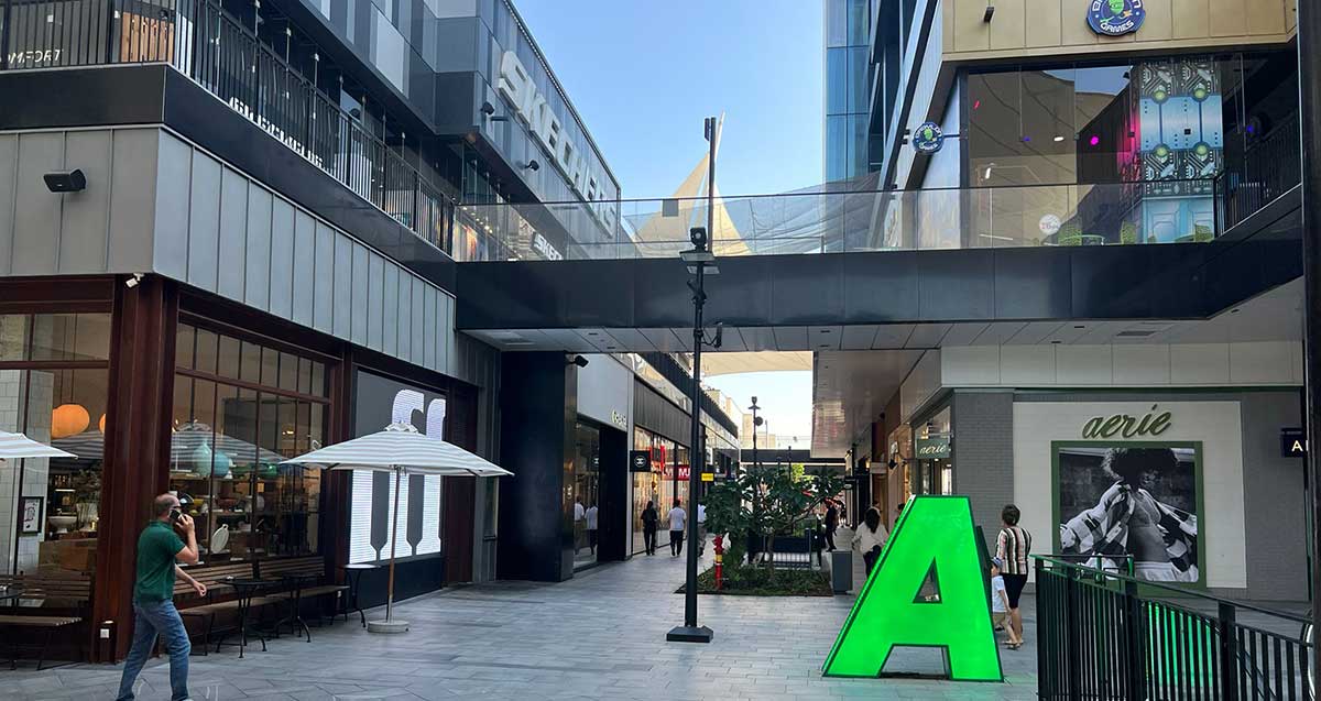 ביג פאשן גלילות. שתי שורות של חנויות בשתי קומות וביניהן רחבה לא מקורה עם גינות, שולחנות, כיסאות וספסלים. לפני אגף ימין שלט גדול וירוק עם האות A
