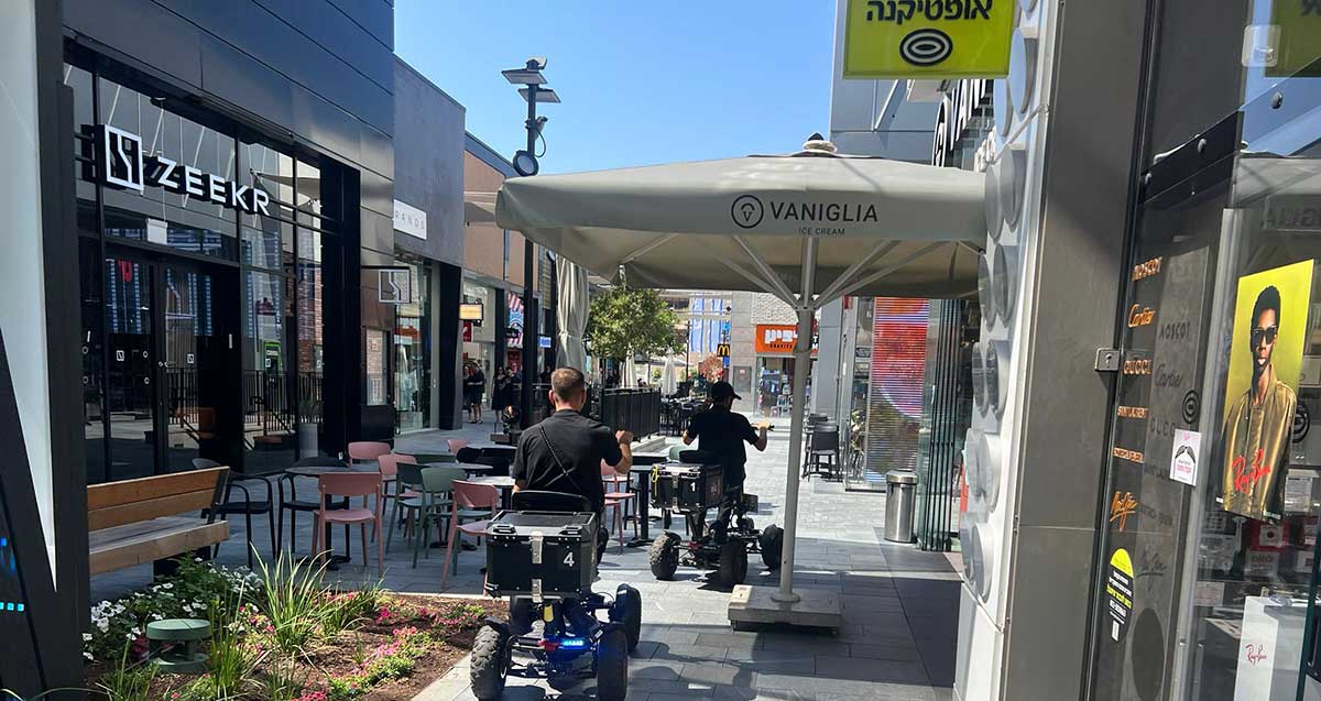 ביג פאשן גלילות. שתי שורות של חנויות בשתי קומות וביניהן רחבה לא מקורה עם גינות, שולחנות, כיסאות וספסלים.