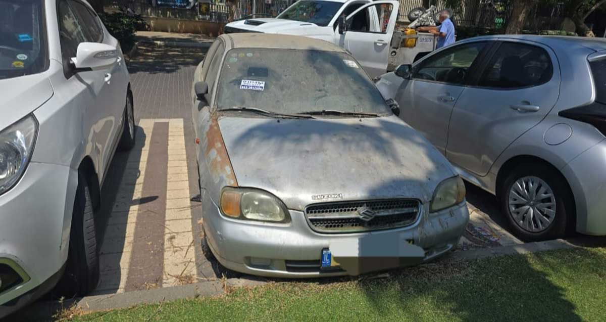 עיריית הרצליה מפנה רכבים נטושים. רכב נטוש עם מדבקה על החלון הקדמי חונה בחנייה. מאחוריו מכונית גרר.