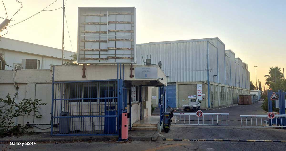 מתחם מפעל אלקו לשעבר ברמת השרון. תמונה של שער הכניסה לרכב, והכניסה להולכי רגל ולידו בניין השומרים בכניסה. ברקע המפעל.