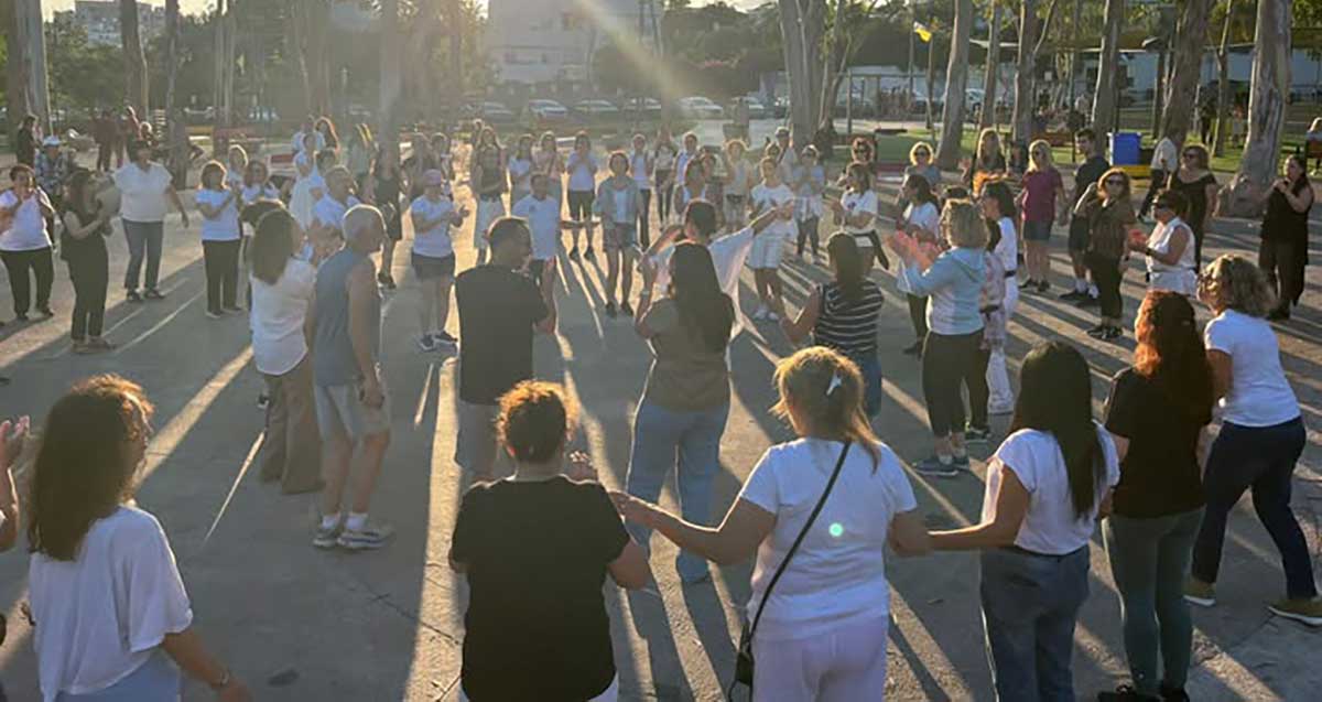 ריקודי עם ברמת השרון. קהל רב רוקד במעגלים בגינה ציבורית. במרכז עומד המרקיד עם מיקרופון.