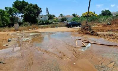 הזיהום במתחם ציר החינוך בהוד השרון. שטח ללא צמחייה מוצף בנוזלים. צינור מים בשטח. ברקע בתי מגורים פרטיים וצמחייה.