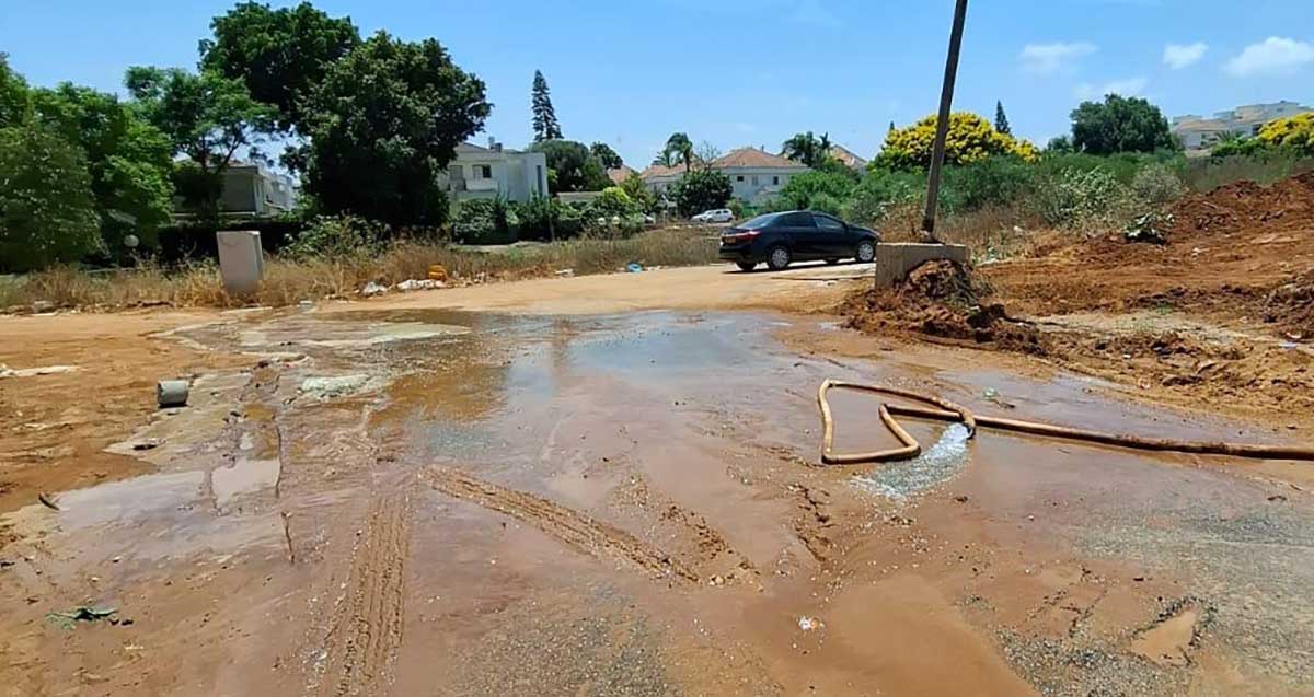 הזיהום במתחם ציר החינוך בהוד השרון. שטח ללא צמחייה מוצף בנוזלים. צינור מים בשטח. ברקע בתי מגורים פרטיים וצמחייה.