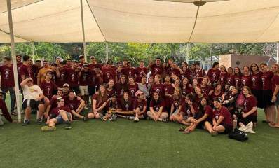 קבוצת בנים ובנות של מחנה הדר מכפר סבא. עומדים ויושבים על דשא סינטטי מתחת לצאליה