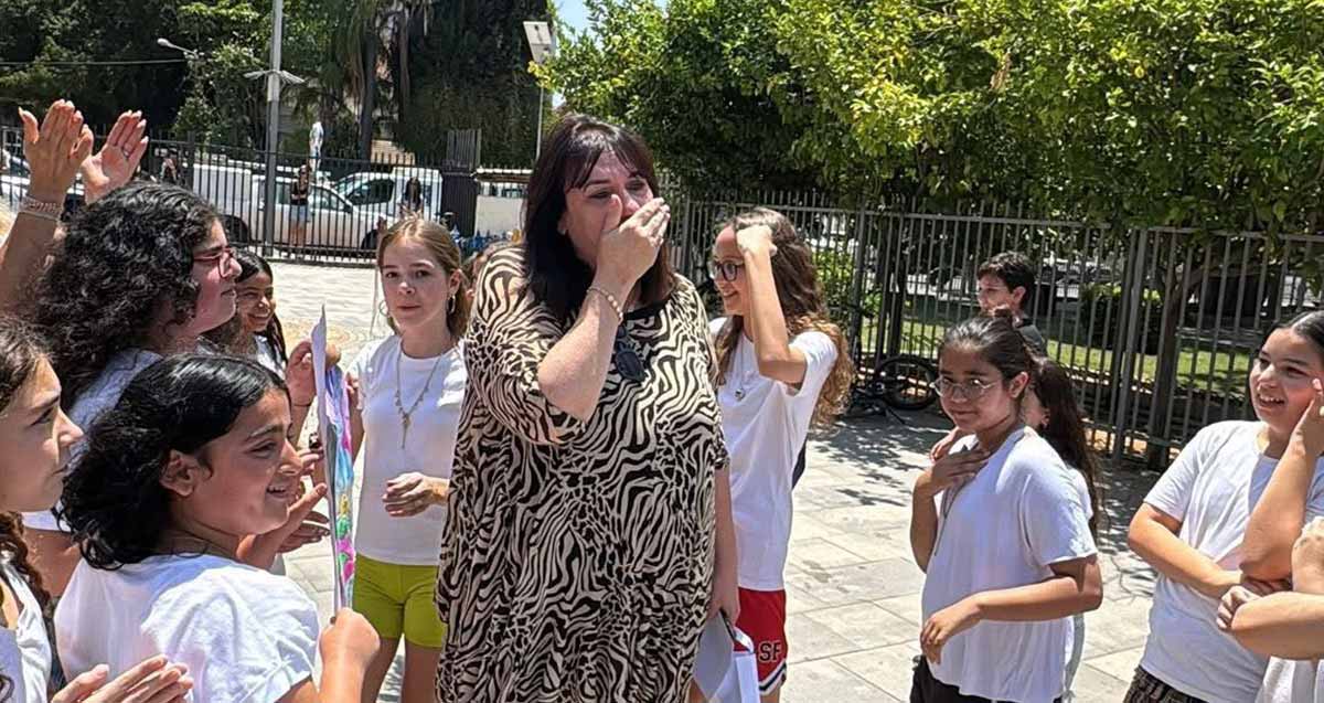 שורות של תלמידים בפרידה מרגשת בהוד השרון מהמנהלת חנה ענבר מילוא. חנה מכסה את פניה מהתרגשות ועוברת בינהן