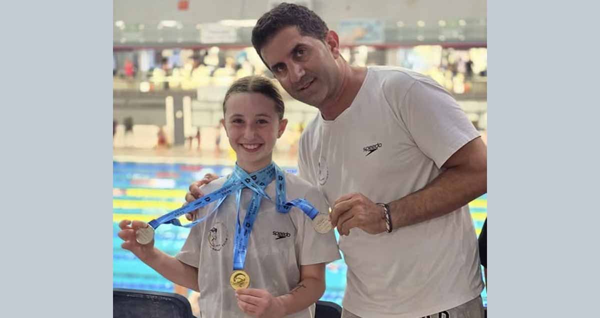 נוי גוטפריד מציגה את המדליות בהן זכתה. אחת מזהב ושניים מכסף, על רקע הבריכה.