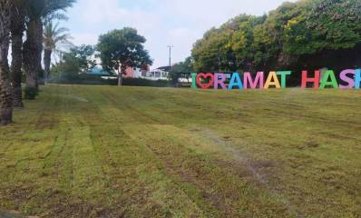 גן החבלים בנווה גן. משטח דשא גדול. שורת דקלים בשמאל. בצד ימין עצים ולפניהם אותיות באנגלית: I LOVE RAMAT HASHARON. במקום המילה LOVE ציור של לב.