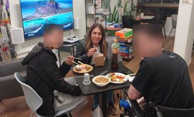 שטרית ושני לוחמים יושבים ליד שולחן עם אוכל בצלחות חד פעמיות ואוחזים שני מקלות לאכילה.