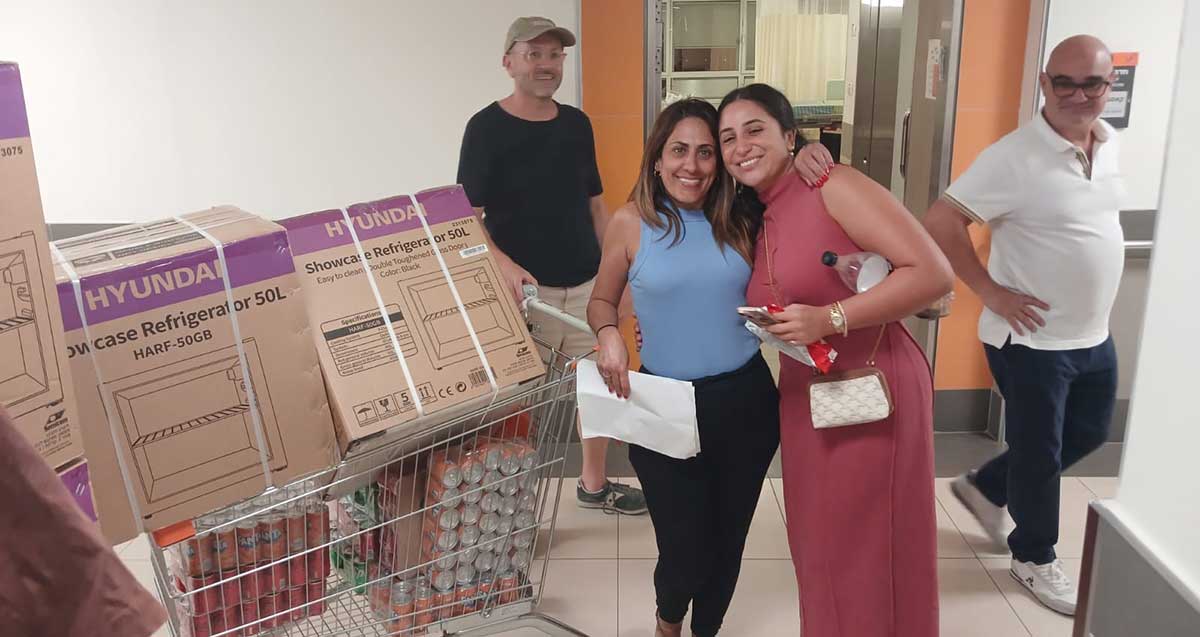 שטרית וצוות מתנדבים עם עגלה של סופרמרקט עמוסה בבקבוקים מפח של שתייה ועליהם שני קרטונים ובהם מקררים קטנים של 50 ליטר.