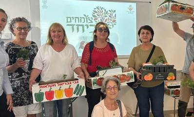 מתנדבי פרויקט "צומחים ביחד" עם ארגזים ובהם שתילים. מאחוריהם על מסך תמונה של צמח וכיתוב: צומחים ביחד.