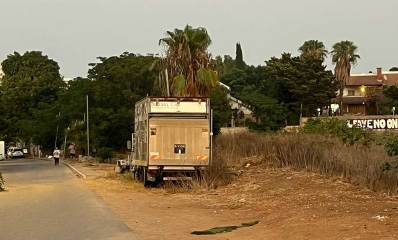 רחוב יבנה מערב ברמת השרון. בצד ימין מגרש ריק עם עשבים ומשאית חונה בו. ברקע עצים גבוהים ואחריהם בניינים גבוהים.