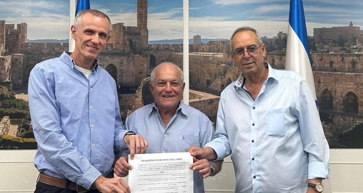 - איציק רוכברגר, שר השיכון חיים כץ וחשב רשות מקרקעי ישראל אוחזים בהסכם החתום. מאחוריהם תמונה של העיר העתיקה בירושלים