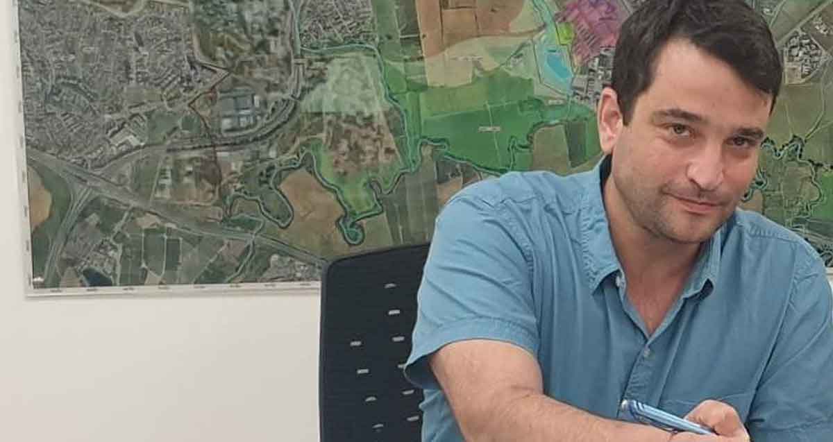 אמיר כוכבי במשרד עם עט בידו. מאחוריו על הקיר מפה של הוד השרון.
