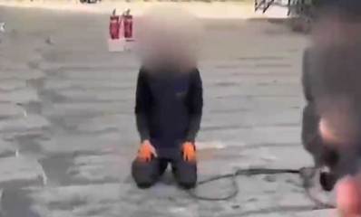 שוטר מכוון אקדח כלפי שוהה בלתי חוקי שכורע על הרצפה עם ידיו על ירכיו. האקדח ופניו של השוהה הבלתי חוקי מטושטשים