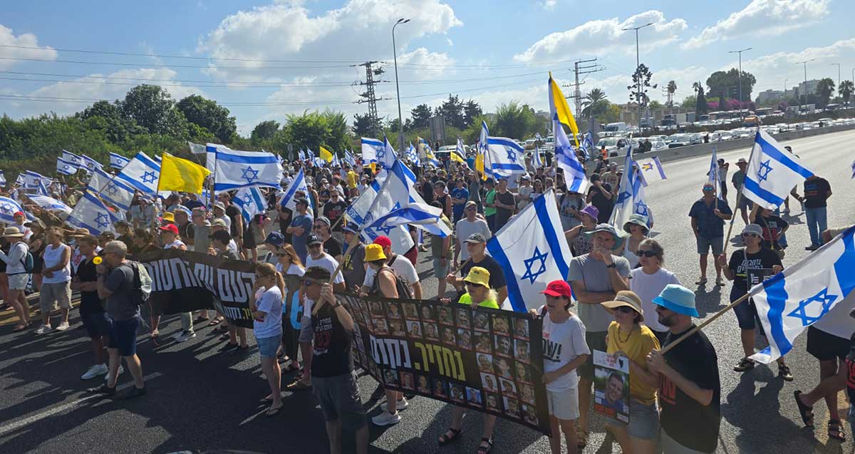 מפגינים עם דגלים צהובים, דגלי ישראל, חוסמים את כביש 5 ונושאים באנר כרזה ענק לשחרור החטופים