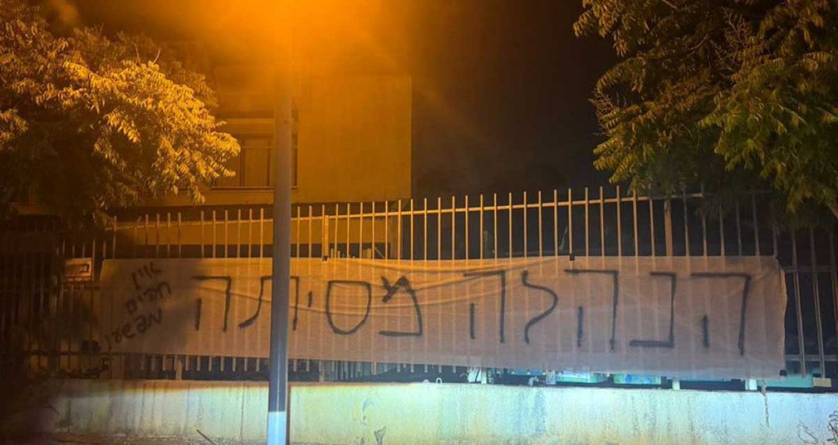 שלט בד תלוי על גדר תיכון גלילי בכפר סבא. בשלט כתוב: הנלה מסיתה. אין חפים מפשע