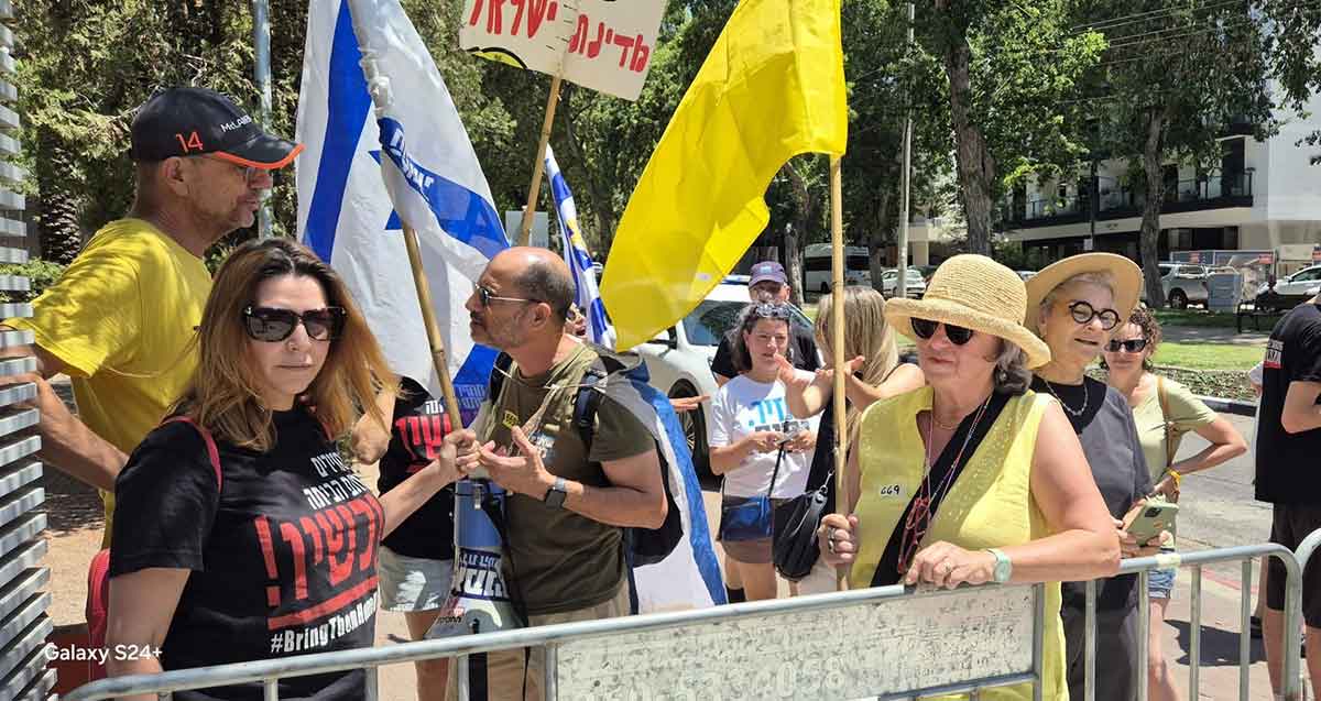 גייל שורש והמפגינים מחוץ לטקס חתימת הסכם הגג, עם דגל המדינה ודגל צהוב.