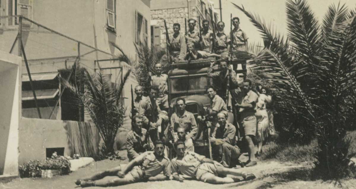 תמונה ישנה בשחור. נוטרים עם נשקים ומדי חאקי ליד משאית
